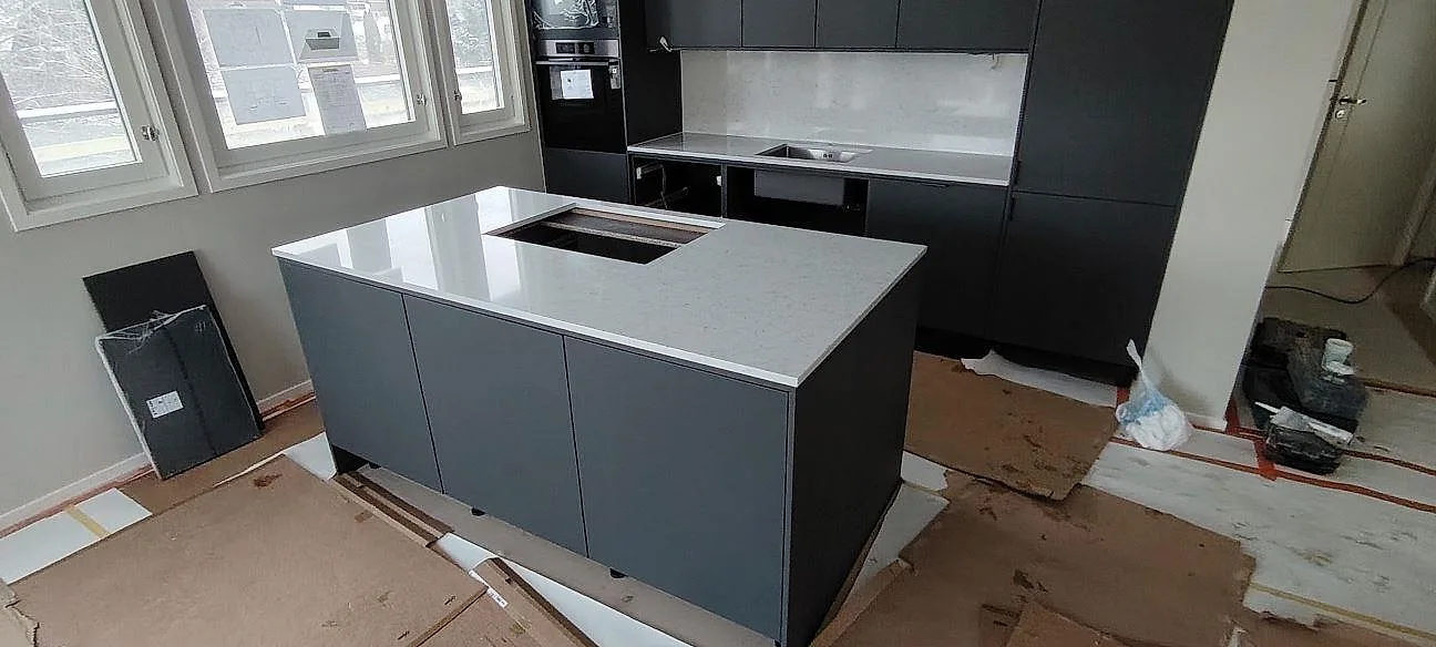 Køkkenbordplade i vitgrå Technistone Noble Carrara, poleret kvartskomposit, på køkkenø og bänkyta längs væggen i ett køkken i Järfälla.