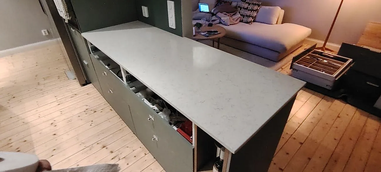 Poleret køkkenbordplade i Technistone Noble Carrara, lys kvartskomposit med grå åretegning, monteret som större plade mot vardagsrummet i Stockholm.