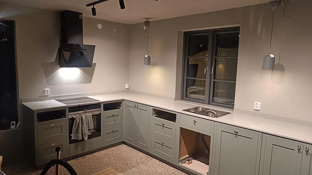 Køkkenbordplade i poleret Technistone Noble Concrete Grey, ljusgrå kvartskomposit, i ett L-format køkken i Bankeryd med låg stänklist.