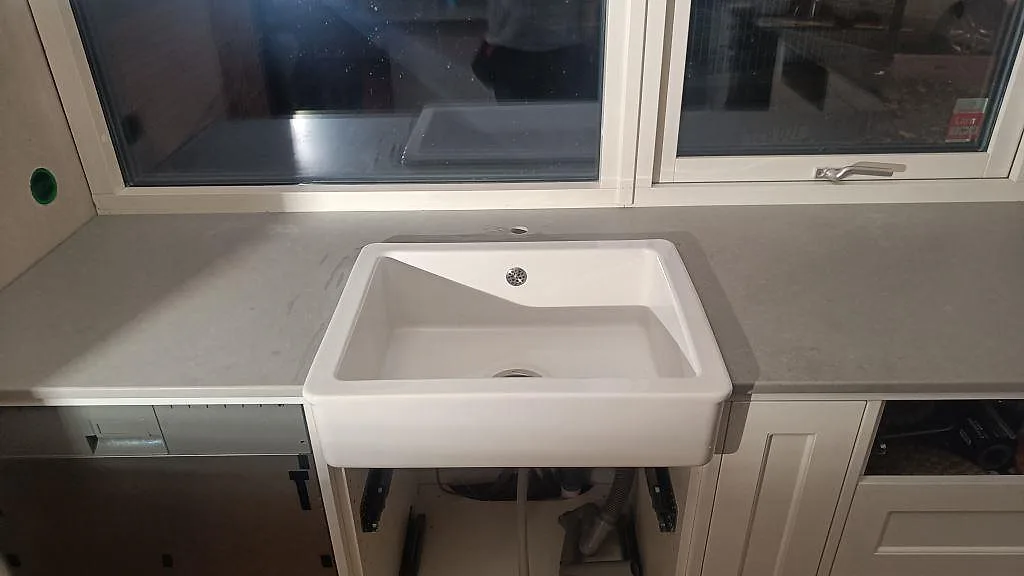 Mat køkkenbordplade i Technistone Noble Concrete Grey rundt om en hvid vask under vindue i ett køkken i Limhamn.