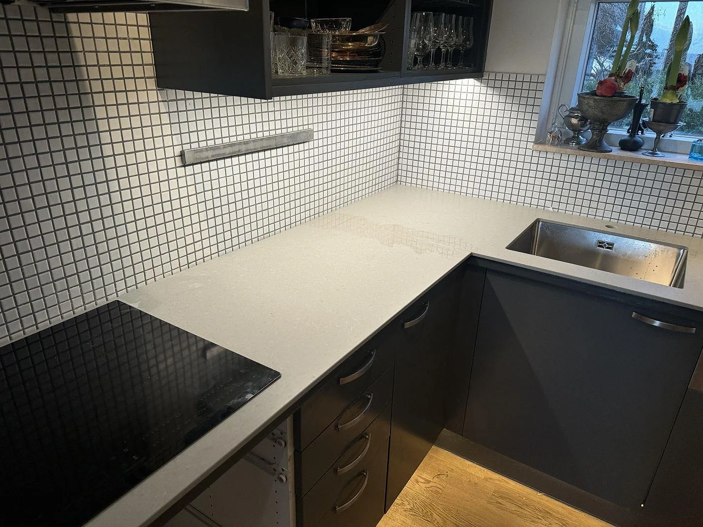 L-formad køkkenbordplade i mat Technistone Noble Concrete Grey, grå kvartskomposit, med rostfri vask og sort kogeplade i ett køkken i Malmö.