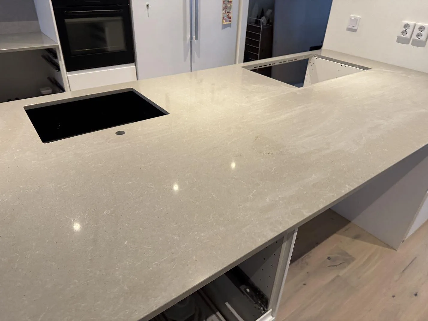 Køkkenbordplade i Technistone Noble Concrete Grey, poleret kvartskomposit, med stor arbetsyta, mørk vask og öppna skabe i ett køkken i Västra Frölunda.