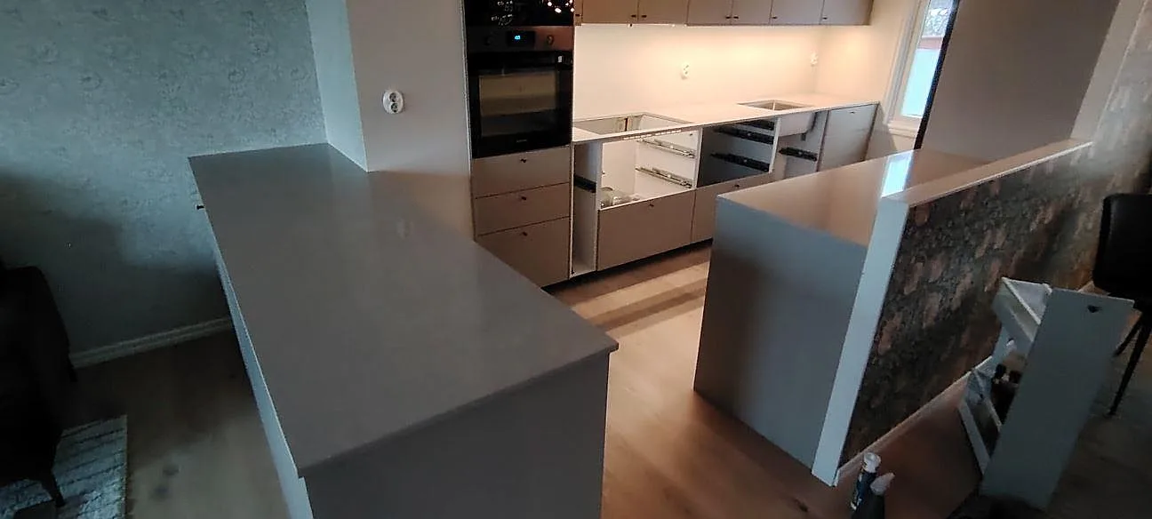Køkkenbordplade i lys Technistone Noble Ivory White, poleret kvartskomposit, på køkkenø og väggbänkar under montering i Enebyberg.