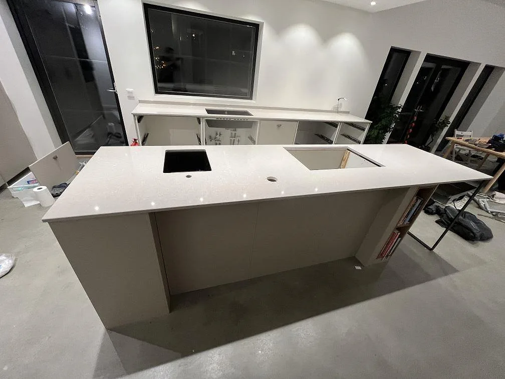 Køkkenø og väggbänk i Technistone Noble Ivory White, poleret kvartskomposit, med synliga udskæring i ett køkken under montering i Ingarö.