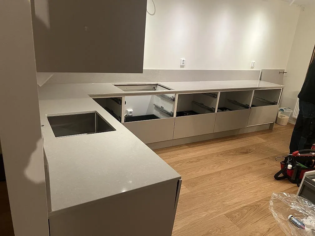 L-formad køkkenbordplade i poleret Technistone Noble Ivory White, lys kvartskomposit, med synlig rostfri vask i ett køkken i Järfälla.