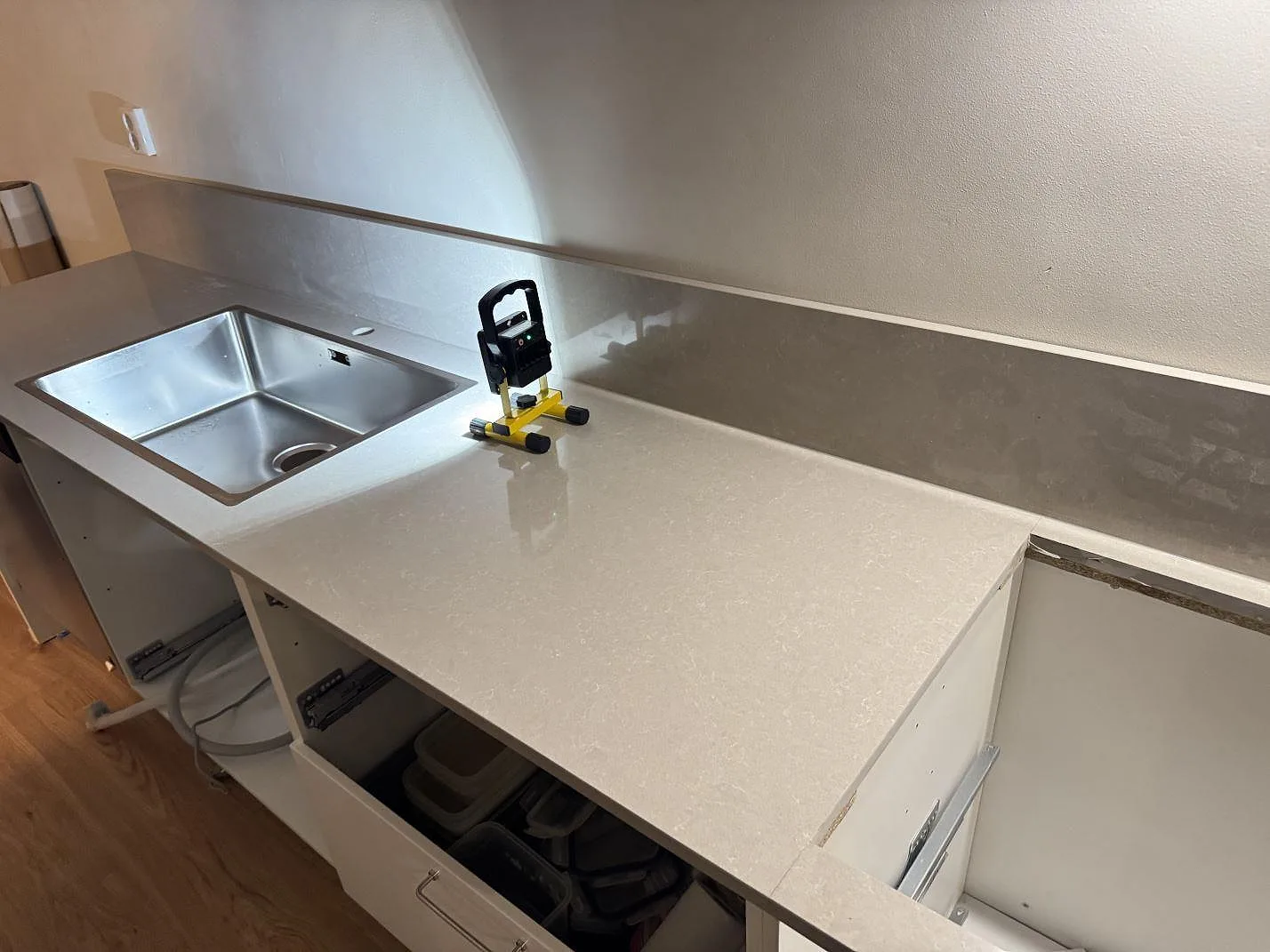 Køkkenbordplade i poleret Technistone Noble Ivory White komposit med rostfri vask, hällöppning og uppvikt stänkkant i ett køkken under montering i Jönköping.