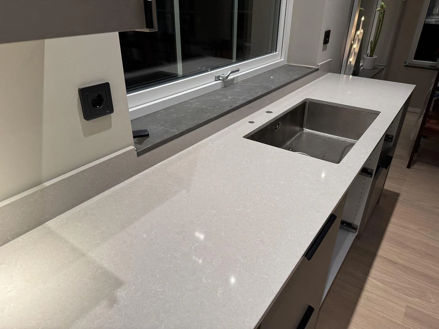 Køkkenbordplade i Technistone Noble Ivory White, poleret lys kvartskomposit, med rostfri vask vid fönsterparti i Kungsbacka.