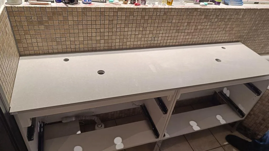 Poleret Bordplade i hvid Technistone Noble Ivory White komposit, monteret over öppna badrumsstommar mot kaklad væg i Limhamn.