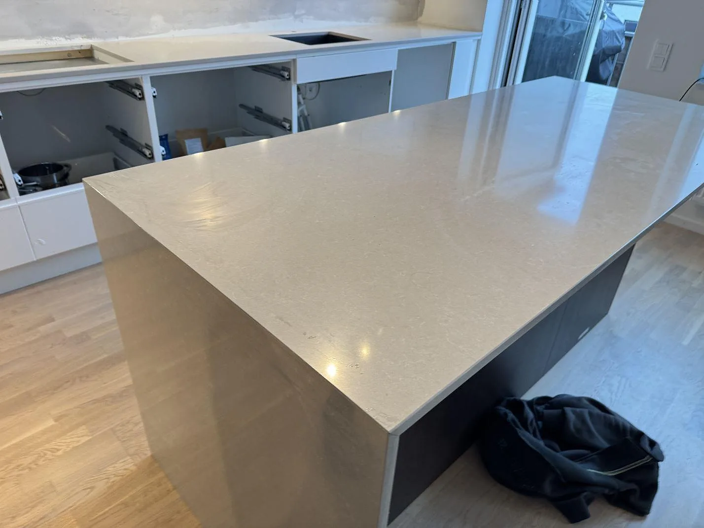 Køkkenø og väggbänk i poleret Technistone Noble Ivory White, lys kvartskomposit, under montering i ett køkken i Malmö.