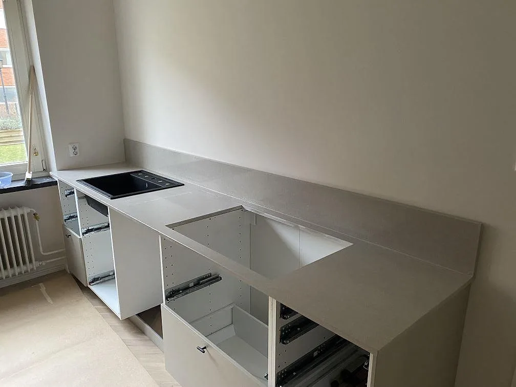 Køkkenbordplade i Technistone Noble Ivory White, poleret kvartskomposit, med uppvikt stänkkant, sort vask og rektangulärt udskæring i ett Malmö-køkken.