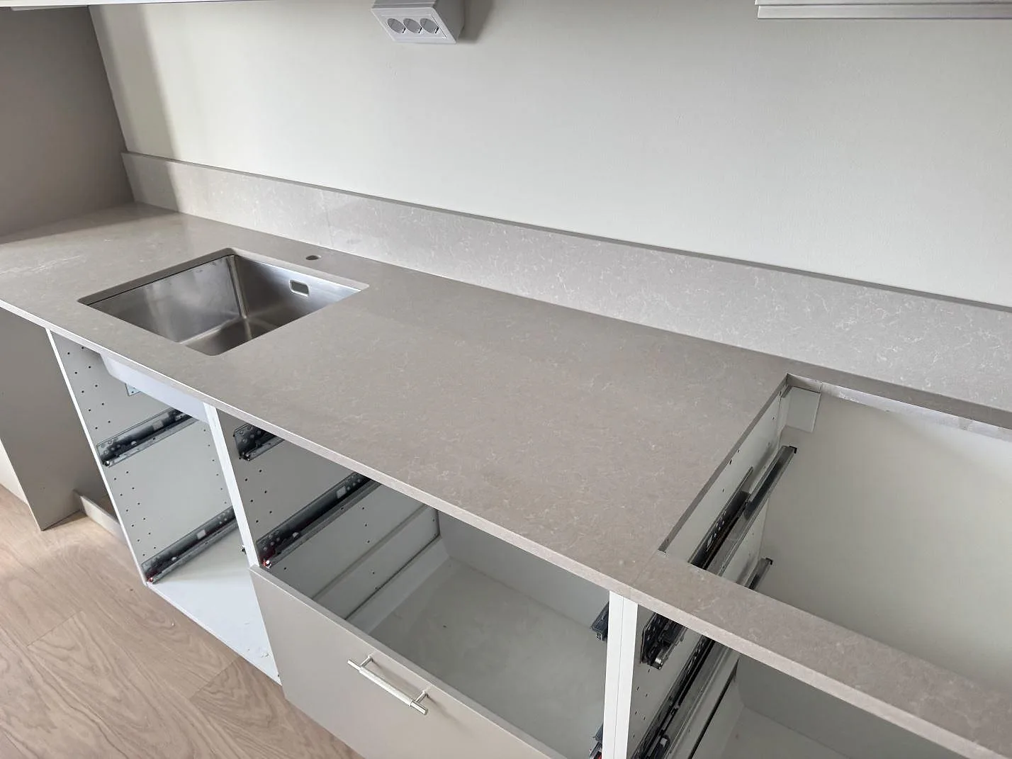 Køkkenbordplade i poleret Technistone Noble Ivory White, lys kvartskomposit, med stænkplade og rostfri vask under montering i Malmö.