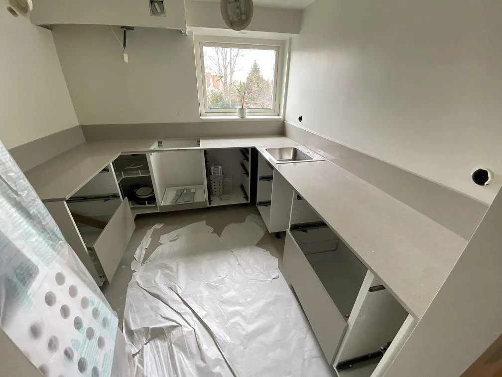 U-format køkken med køkkenbordplade i Technistone Noble Ivory White, poleret kvartskomposit, låg stänkkant, rostfri vask og udskæring for kogeplade i Malmö.