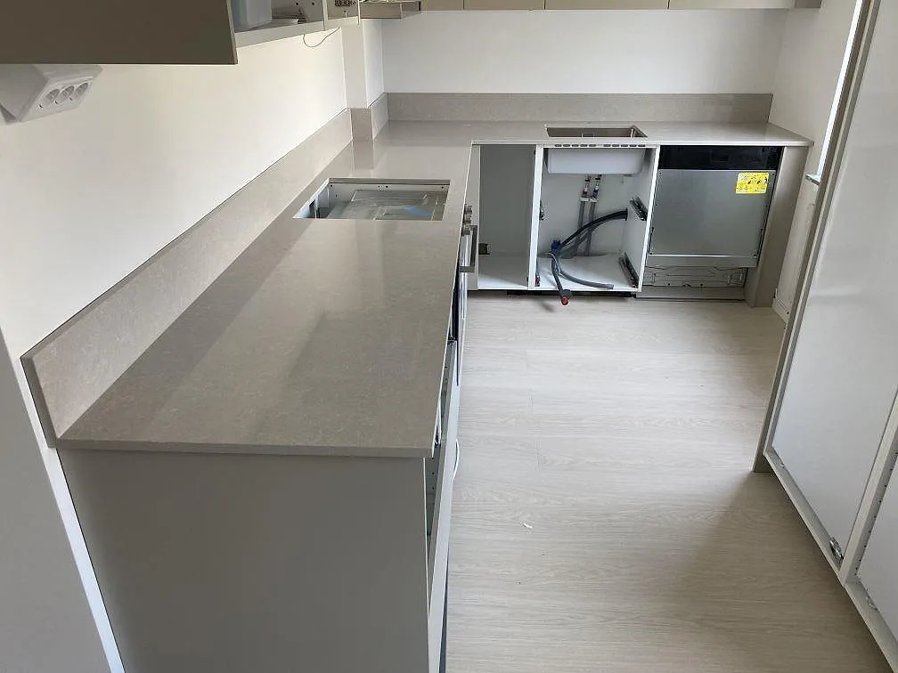 Køkkenbordplade i poleret Technistone Noble Ivory White kvartskomposit med låg stänkkant i ett L-format køkken under montering i Malmö.