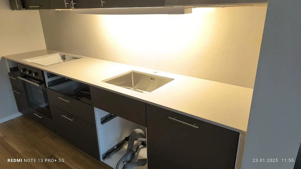 Køkkenbordplade i poleret Technistone Noble Ivory White, 20 mm kvartskomposit, med underlimmad vask i ett køkken med mørke skabe i Nacka.