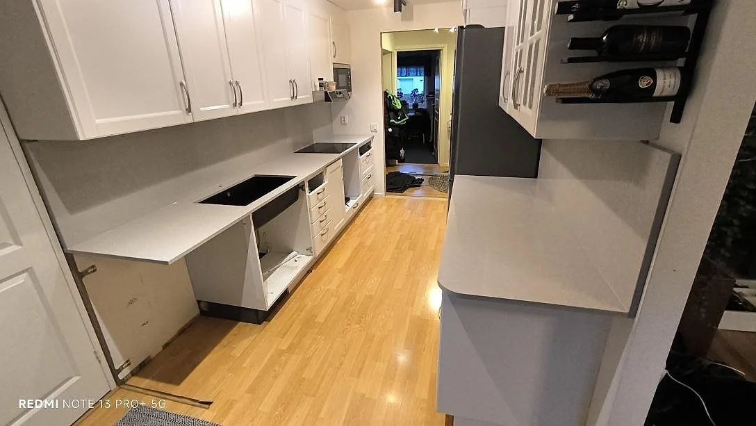 Køkkenbordplade i Technistone Noble Ivory White, poleret lys kvartskomposit, längs två bänkrader med vita skabe i Norrköping.