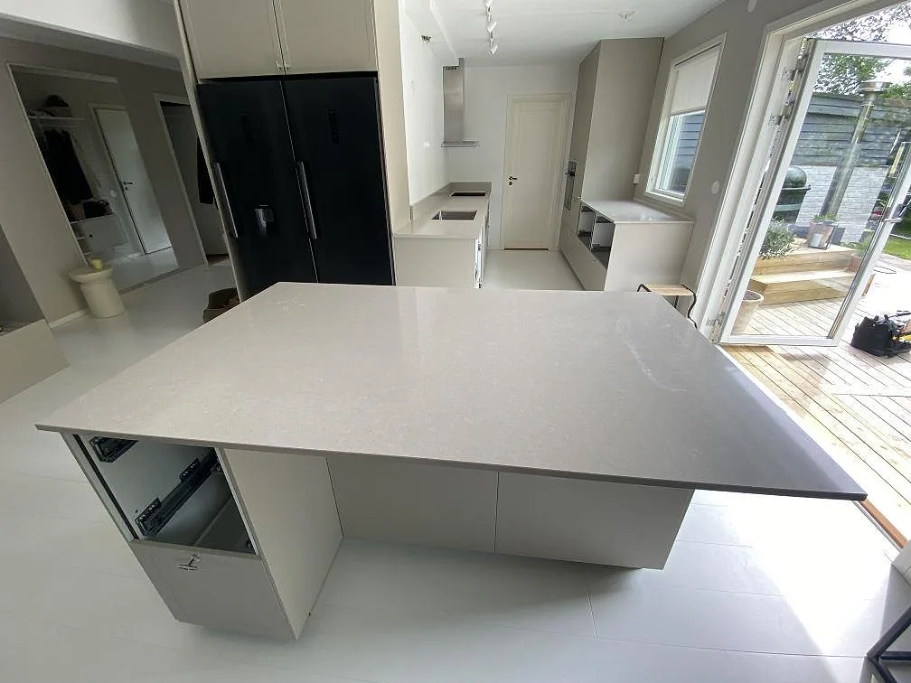 Køkkenbordplade og køkkenø i poleret Technistone Noble Ivory White, hvid komposit, i ett køkken i Simrishamn.