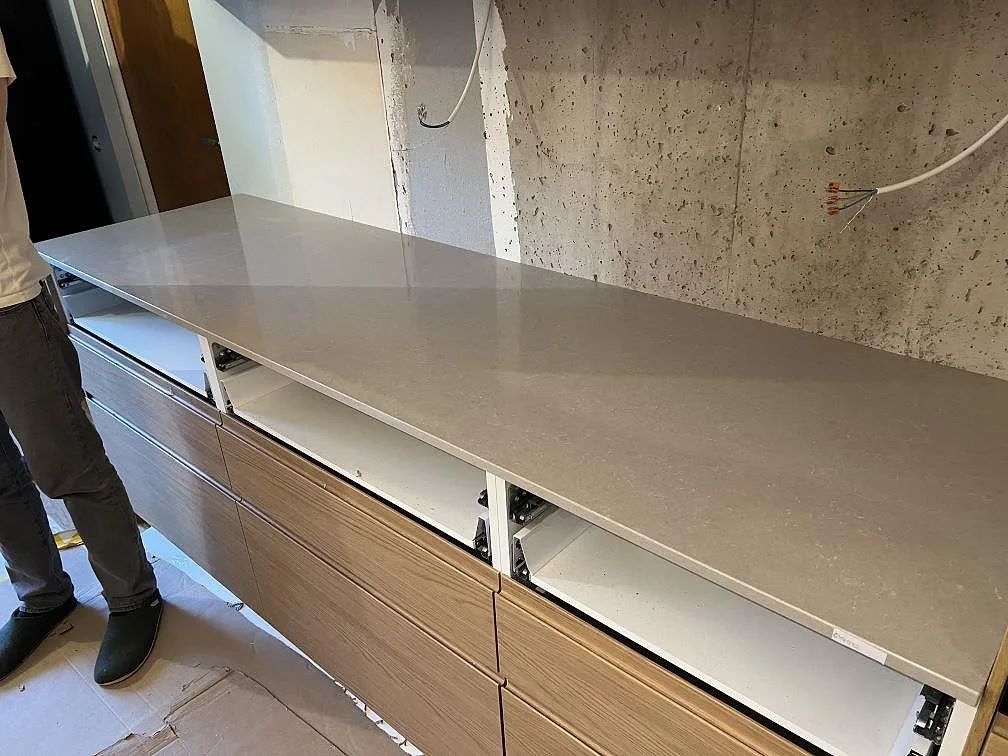 Lang køkkenbordplade i lys Technistone Noble Ivory White, poleret kvartskomposit, på träinredning og öppna skabe i Sköndal.