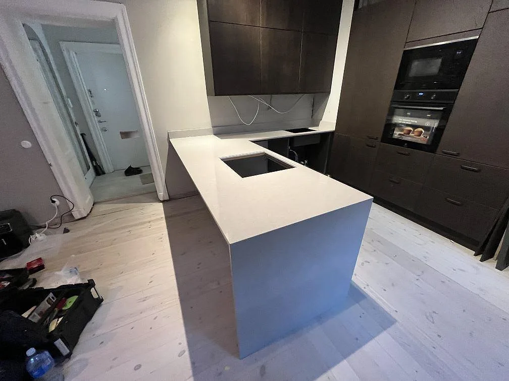 Køkkenbordplade og køkkenø i Technistone Noble Ivory White, poleret hvid komposit, med synliga udskæring under montering i Stockholm.