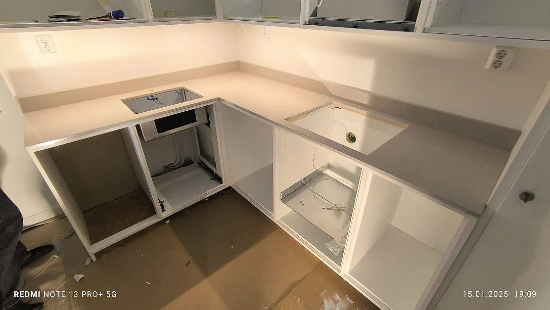 Køkkenbordplade i lys Technistone Noble Ivory White, poleret kvartskomposit, med synliga udskæring og låg väggkant i ett køkken under montering i Stockholm.