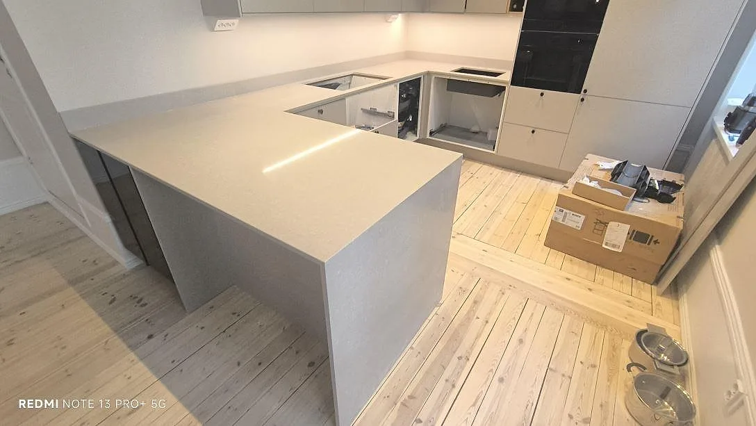 Køkkenbordplade i Technistone Noble Ivory White, poleret lys kvartskomposit i 20 mm, på stor køkkenø og väggbänk med stänkkant under montering i Stockholm.