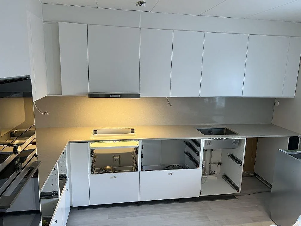 L-formad køkkenbordplade i Technistone Noble Ivory White, poleret kvartskomposit, med stænkplade i ett køkken i Sturefors.