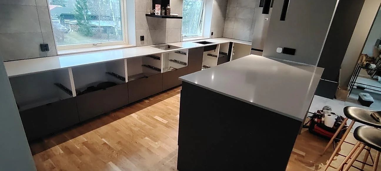 Køkkenbordplade og køkkenø i poleret Technistone Noble Ivory White, lys kvartskomposit, under montering i ett køkken i Torshälla.