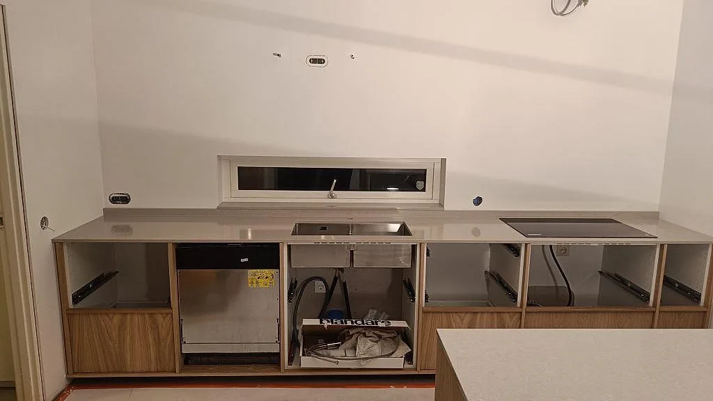 Køkkenbordplade i lys Technistone Noble Ivory White, poleret 20 mm kvartskomposit, med diskzon og hällzon i ett køkken under montering i Trelleborg.