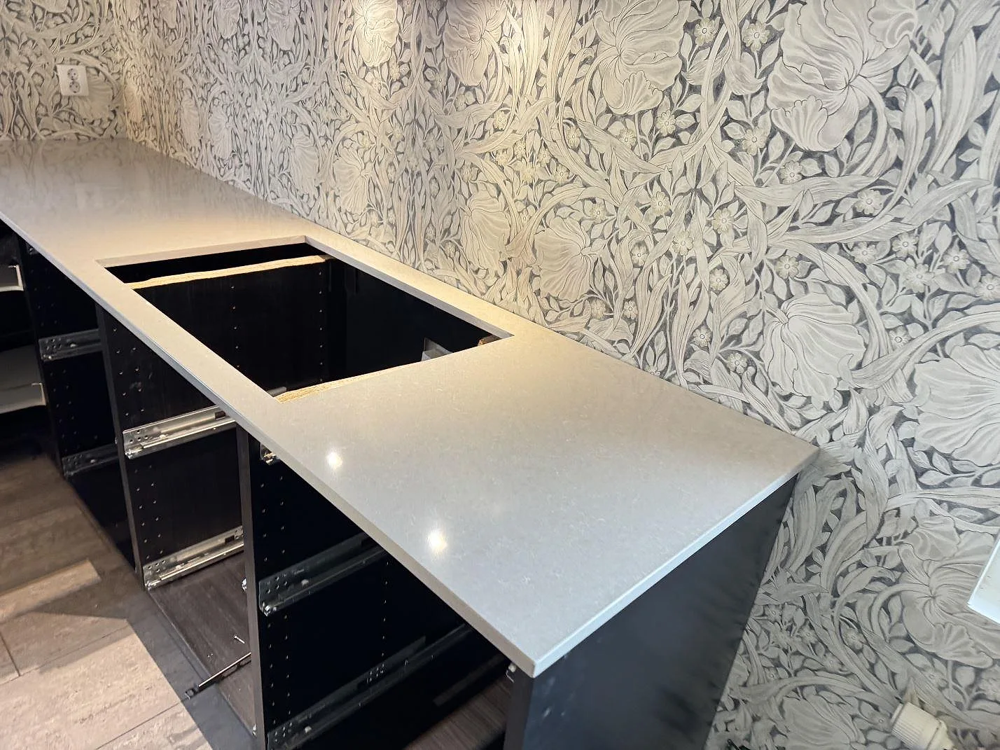 Køkkenbordplade i Technistone Noble Ivory White, poleret kvartskomposit, med rektangulärt udskæring og öppna mørke skabe i ett køkken i Trelleborg.