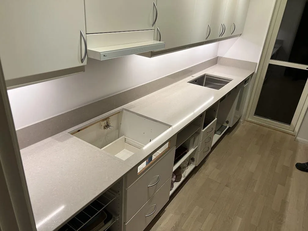 L-formad køkkenbordplade i Technistone Noble Ivory White, poleret lys kvartskomposit med synliga udskæring og stänkkant, monteret i ett køkken i Tullinge.
