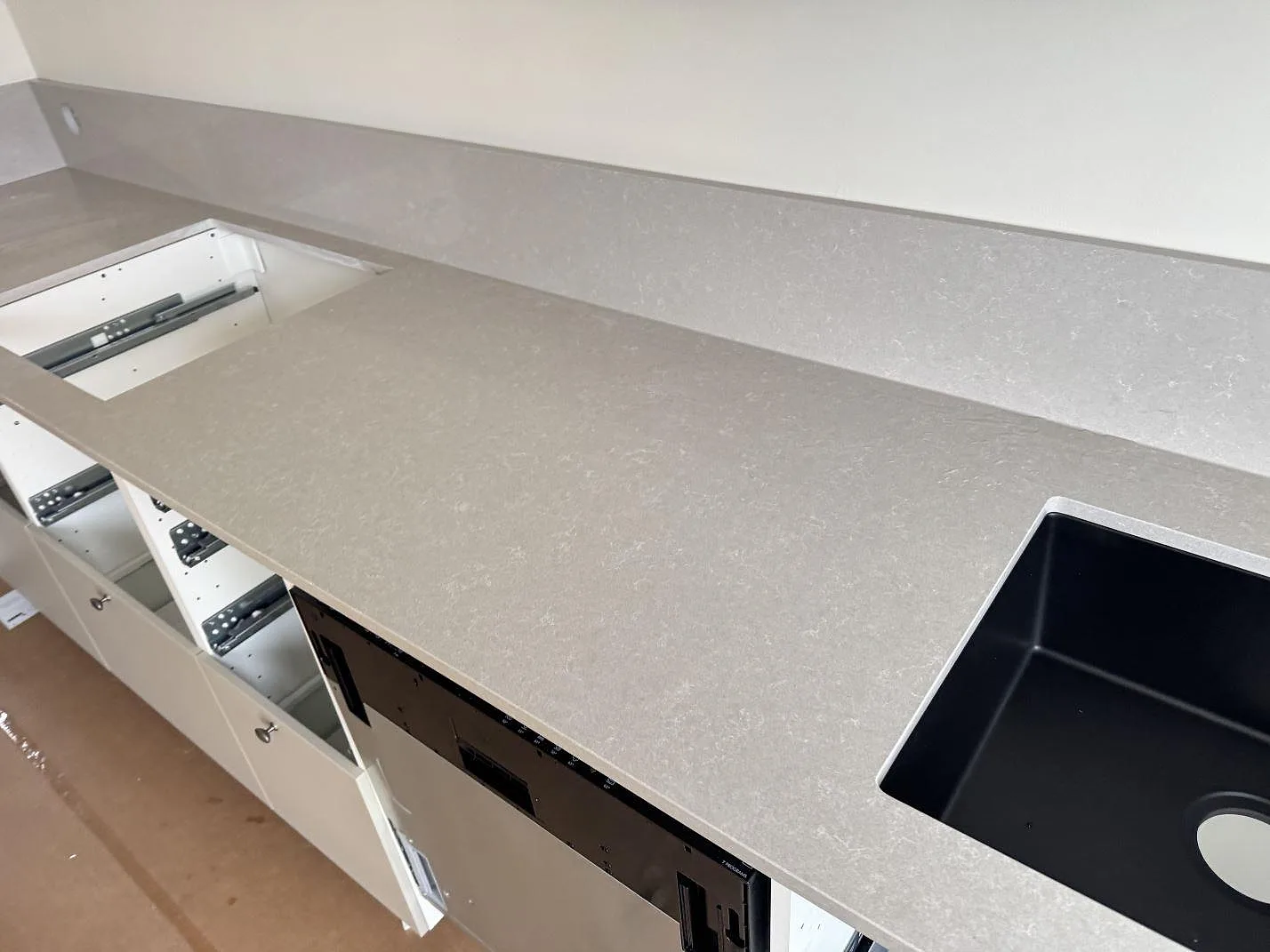 Poleret køkkenbordplade i Technistone Noble Ivory White, kvartskomposit, med sort vask, hällurtag og låg stänkkant i ett køkken i Vänersborg.