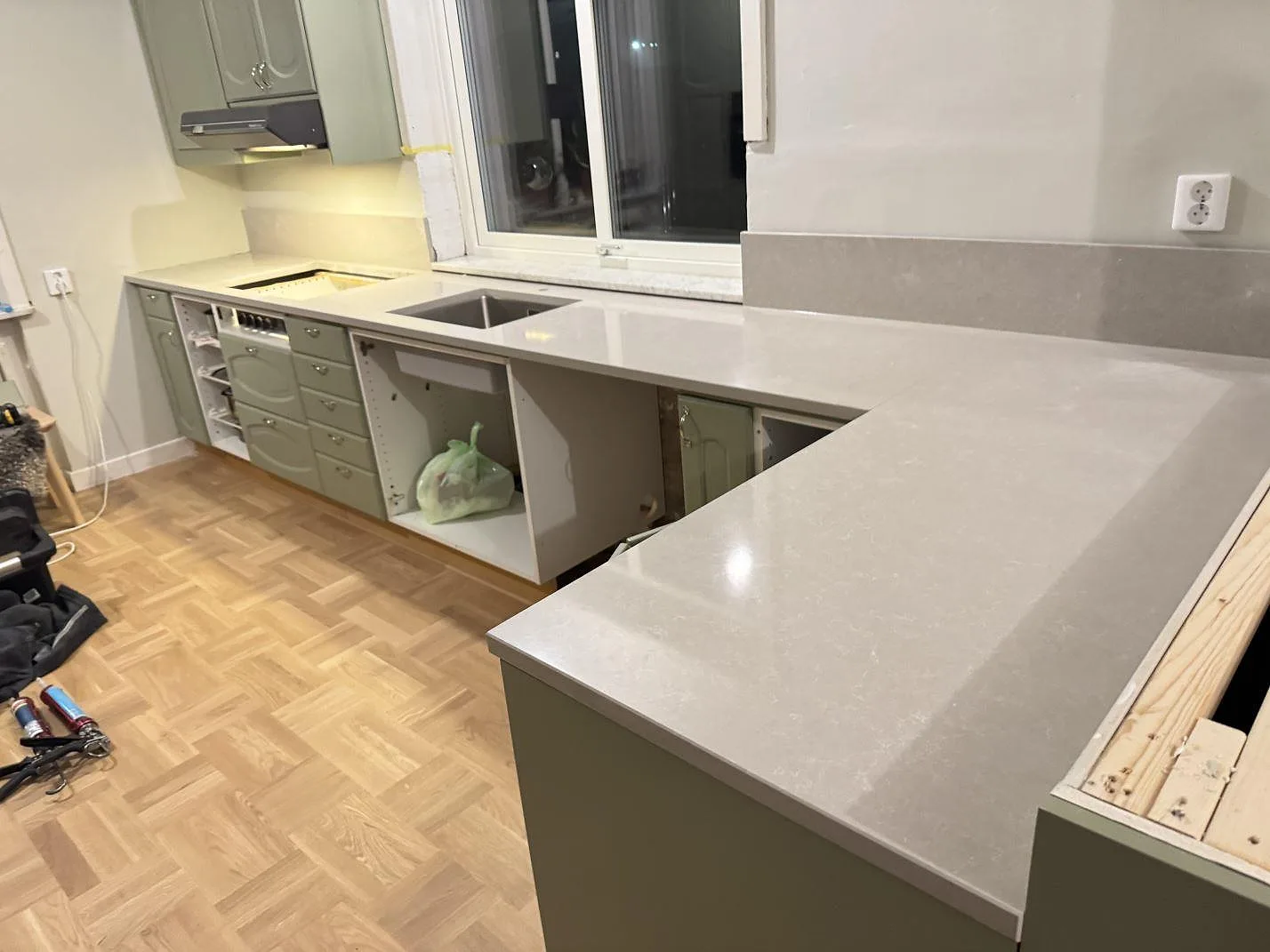 L-format køkken i Veberöd med køkkenbordplade i poleret Technistone Noble Ivory White, lys kvartskomposit, låg stänkkant, rostfri vask og hällurtag under montering.