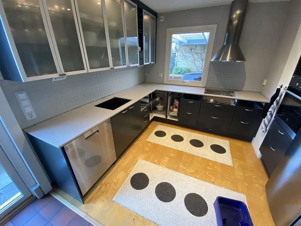 Køkkenbordplade i poleret Technistone Noble Ivory White, lys kvartskomposit, i ett L-format køkken med sort vask og kogeplade i Vellinge.