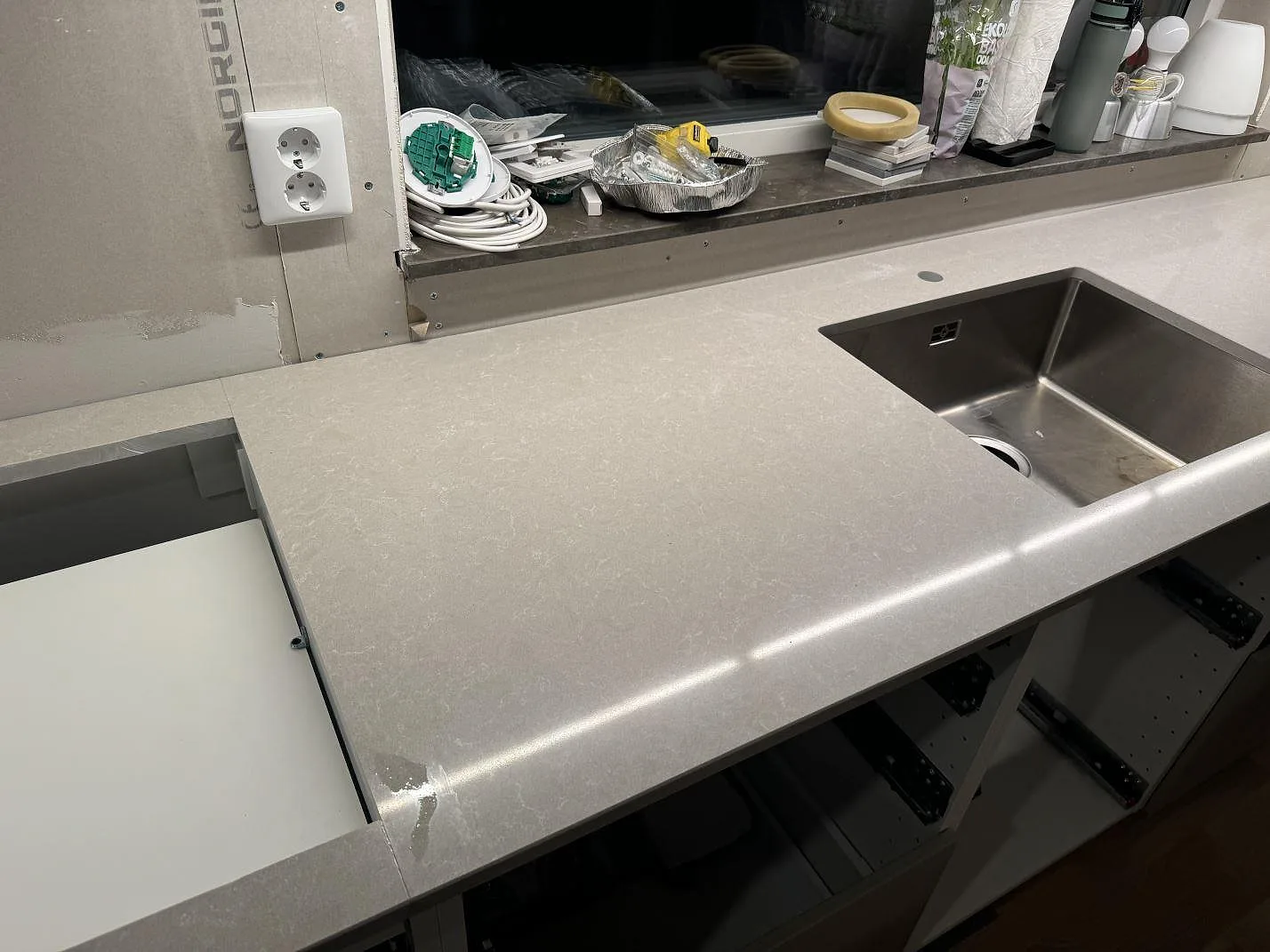 Køkkenbordplade i poleret Technistone Noble Ivory White, lys kvartskomposit, med rostfri vask og hällurtag i ett køkken under montering i Vintrie.