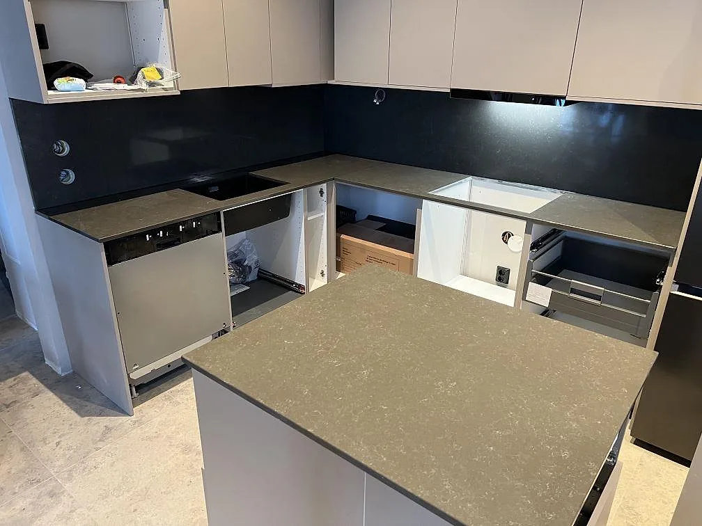 Køkkenø og U-formad køkkenbordplade i poleret Technistone Noble Pietra Grey, kvartskomposit, med förberedda udskæring i ett køkken under montering i Ingarö.