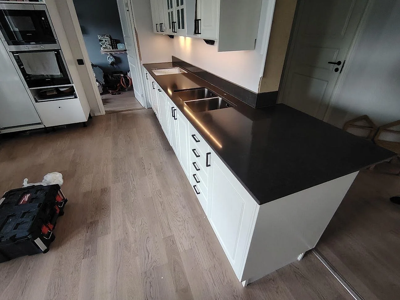 Køkkenbordplade i poleret Technistone Noble Pietra Grey, mörkgrå kvartskomposit, med rostfri vask og uppvikt stänkkant i ett køkken i Vendelsö.