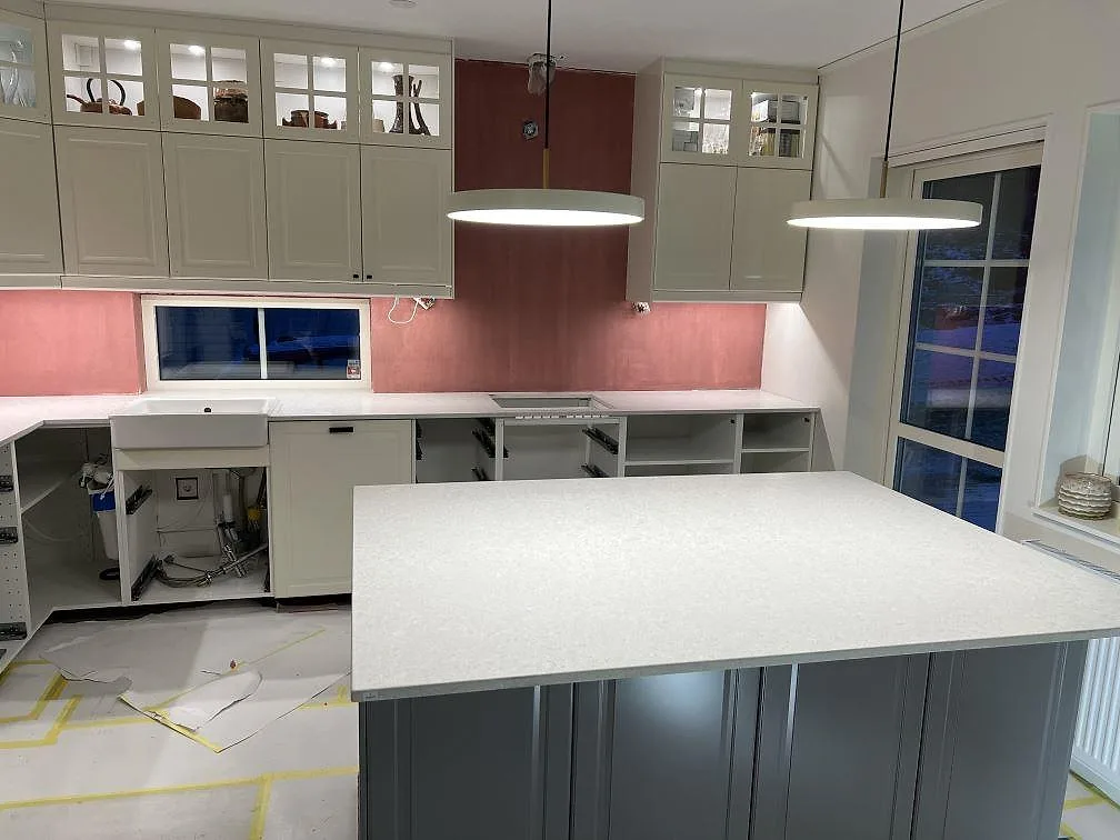 Køkkenbordplade i ljusgrå Technistone Noble Quartzite, mat kvartskomposit, med stor køkkenø og väggbänk under montering i Brottby.