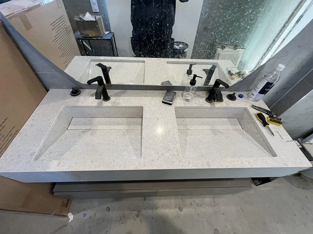 Installerad poleret badrumsbänkskiva i Technistone Noble Quartzite komposit med två rektangulära tvättställsöppningar, spegel og svarta armatur i Huddinge.