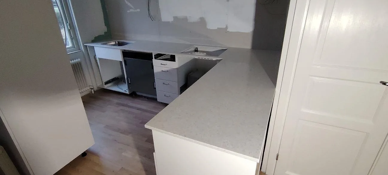 Køkkenbordplade i lys Technistone Noble Quartzite, poleret kvartskomposit, med L-formad bänkyta og synliga udskæring i ett køkken i Västerås.