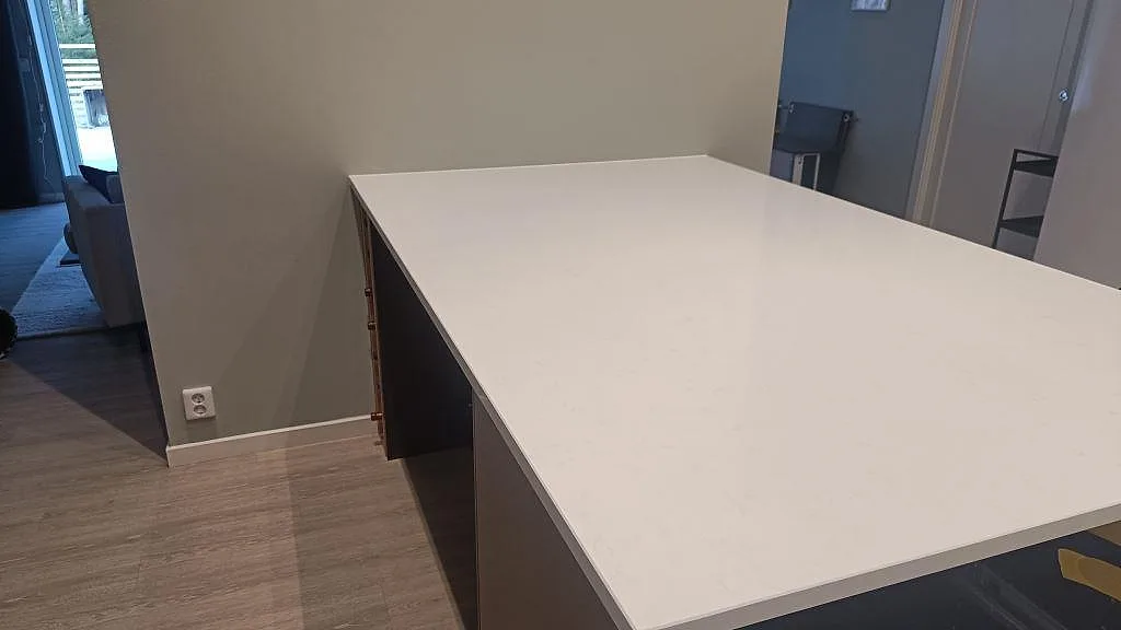 Køkkenbordplade i poleret Technistone Noble Supreme White, hvid kvartskomposit, monteret på mørke köksstommar i Floda.