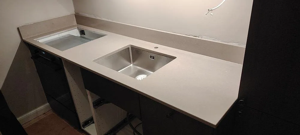 Køkkenbordplade i poleret Technistone Noble Troya, 20 mm kvartskomposit, med rostfri vask, hällöppning og låg stänkkant i Sundbyberg.