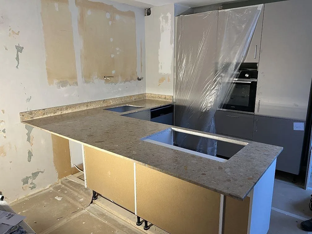 Køkkenbordplade og køkkenø i mat Terrazzo Breccia Oniciata, 20 mm, med udskæring for vask og induktionshäll i ett køkken i Stockholm.