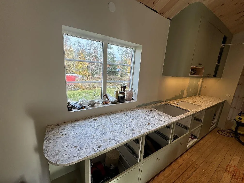 Køkkenbordplade i mat Terrazzo Calacatta, 20 mm, monteret längs væggen under fönstret i ett køkken i Kode.