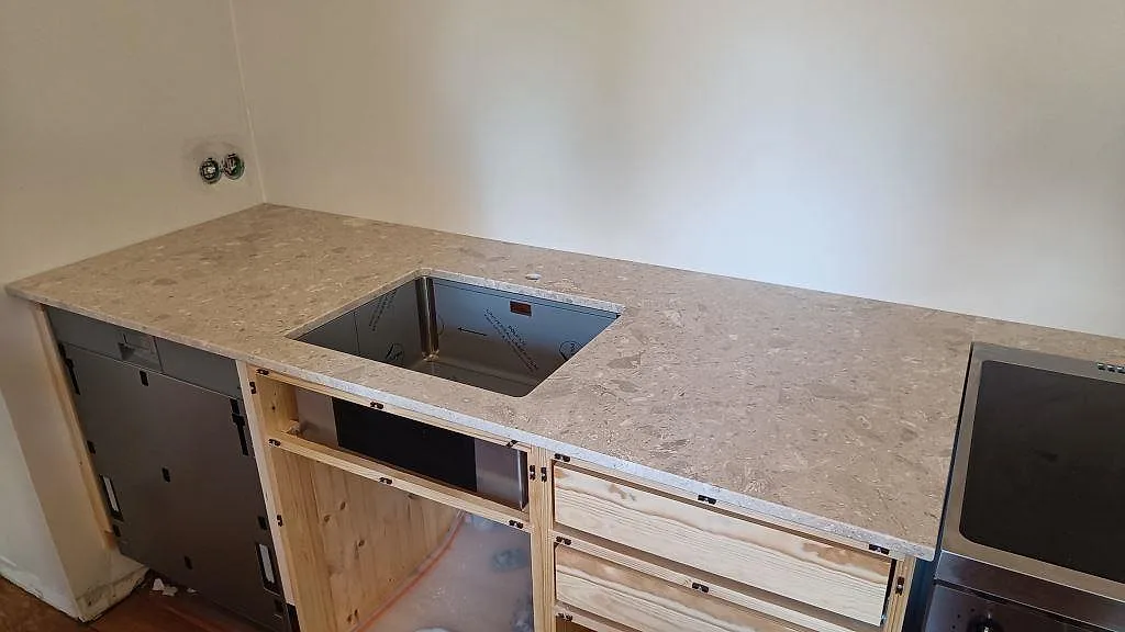 Køkkenbordplade i mat Terrazzo Perlato Royal, beige terrazzo, med diskhozon og fristående komfur i ett køkken under montering i Malmö.