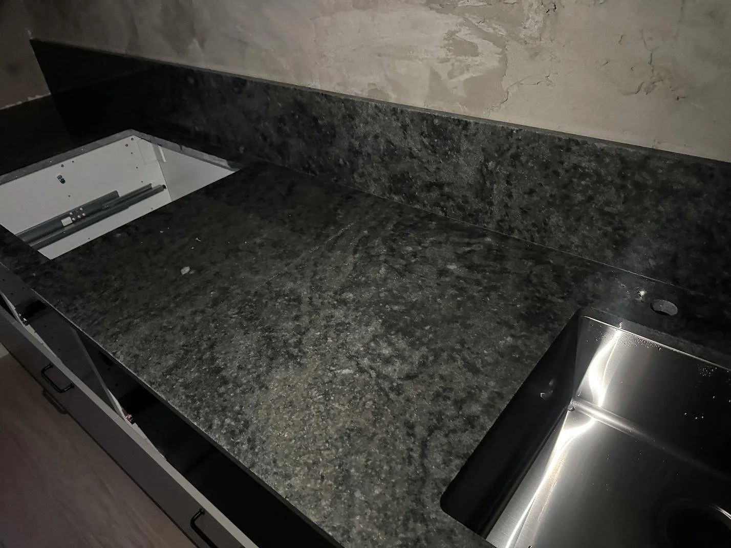 Køkkenbordplade i Verde Savana granit, poleret, med uppvikt stänkkant og rostfri vask under montering i Malmö.