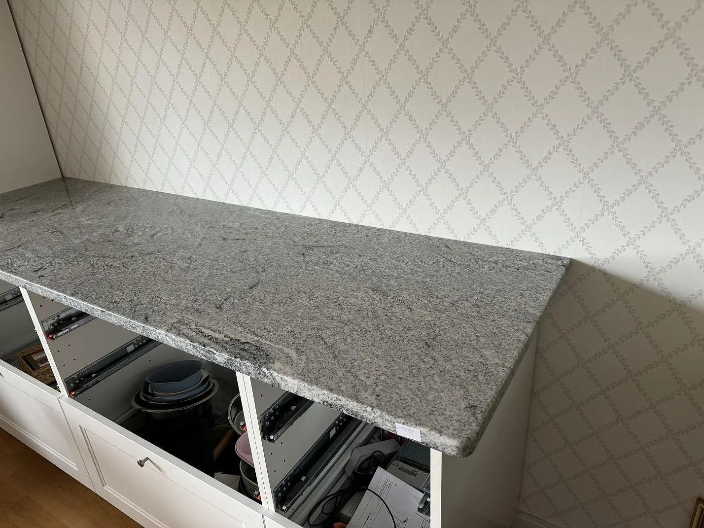 Køkkenbordplade i 30 mm poleret Viscont White-granit på vita skåpstommar mot mönstrad væg i Bjärred.