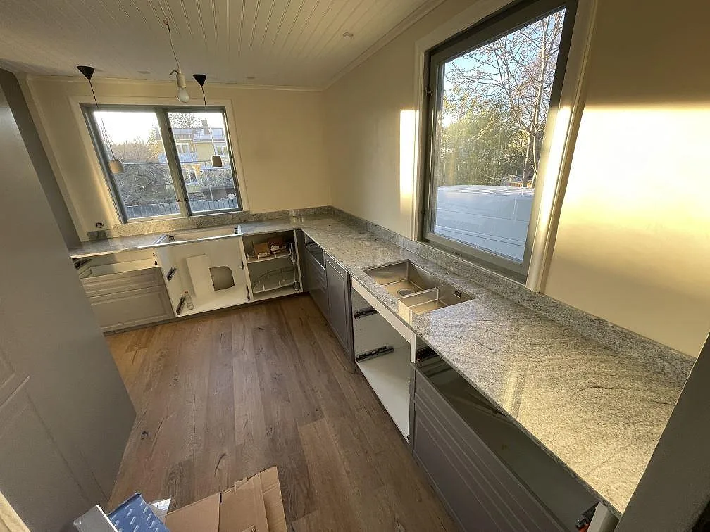 U-formad køkkenbordplade i poleret Viscont White granit, 20 mm, med synliga udskæring vid diskplatsen og stora vindue i ett køkken under montering i Bromma.