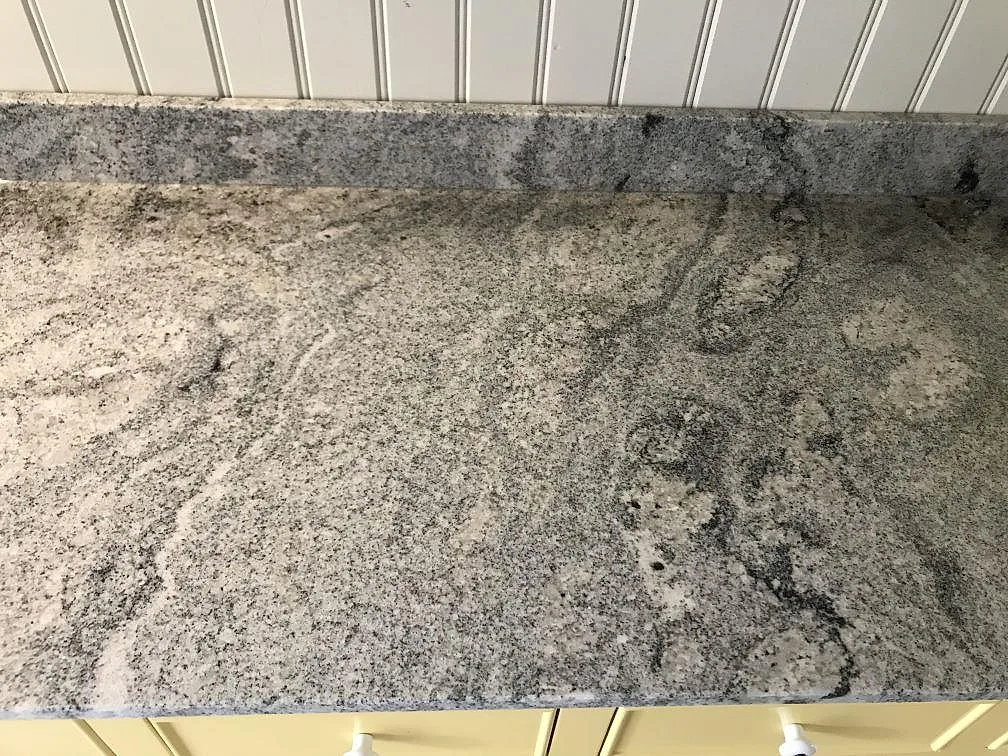 Køkkenbordplade i Viscont White granit, poleret, med kraftig grågrön åretegning längs en lige bänklinje i ett køkken i Helsingborg.