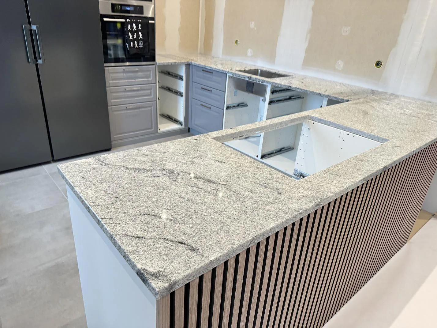 Køkkenbordplade og køkkenø i poleret granit Viscont White i ett køkken under montering i Kävlinge.