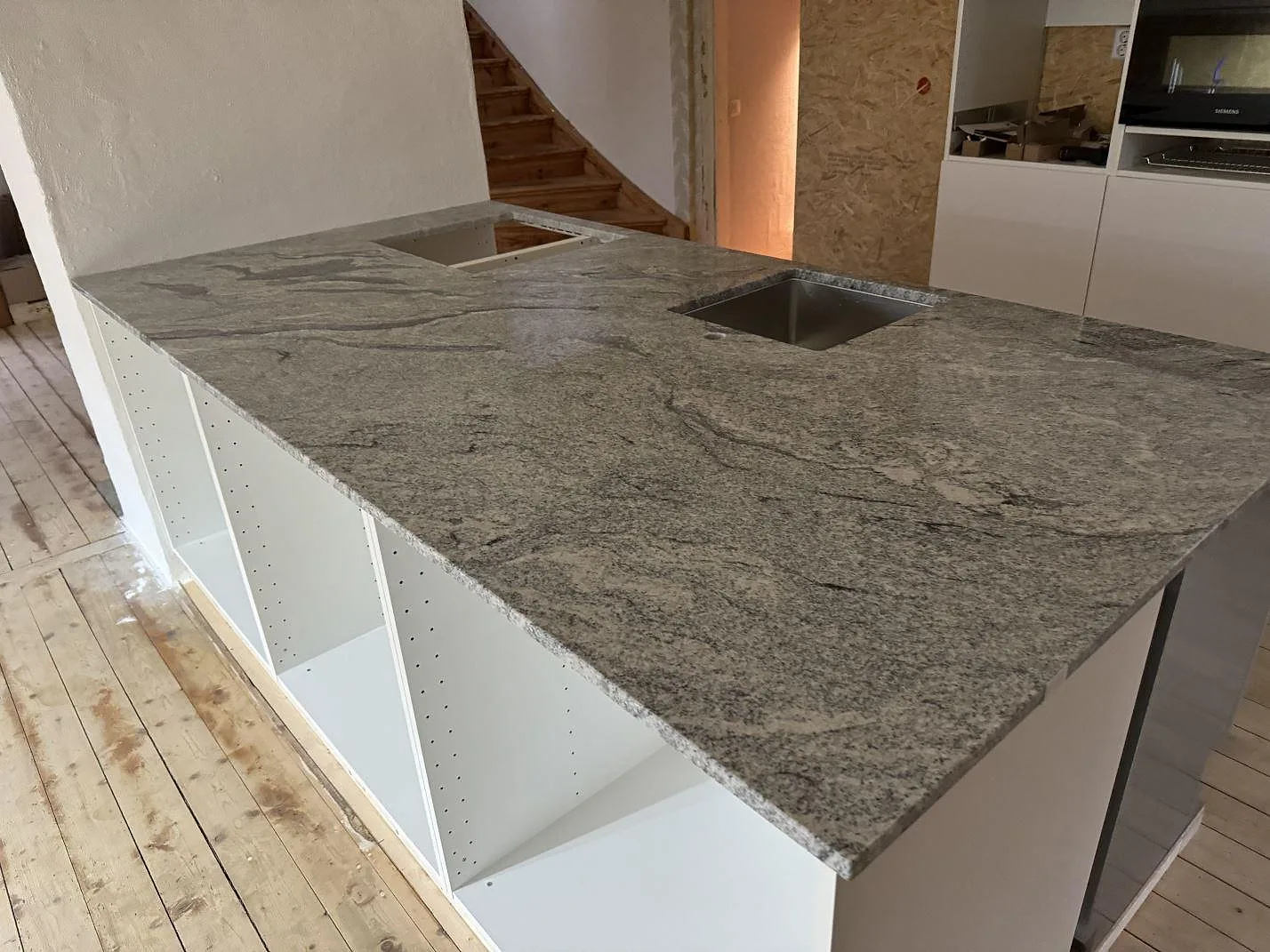 Køkkenbordplade i poleret Viscont White-granit med grå åretegning, vask og udskæring for kogeplade under montering i ett køkken i Olofström.