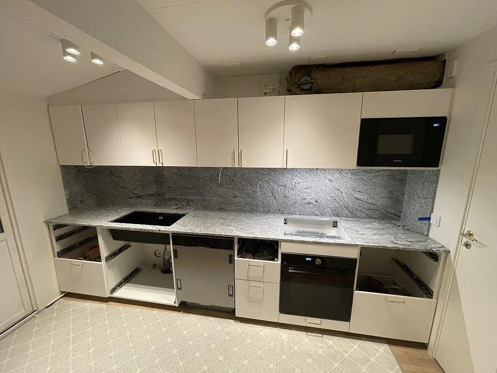 Køkkenbordplade i granit Viscont White, poleret, med heltäckande granitstänkvägg og underlimmad sort vask i ett køkken under montering i Sollentuna.